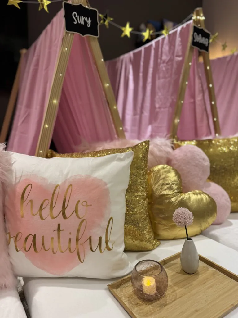 Gold and pink slumber party setup with blush teepees, satin pillows, fairy lights, and personalized sleepover décor.